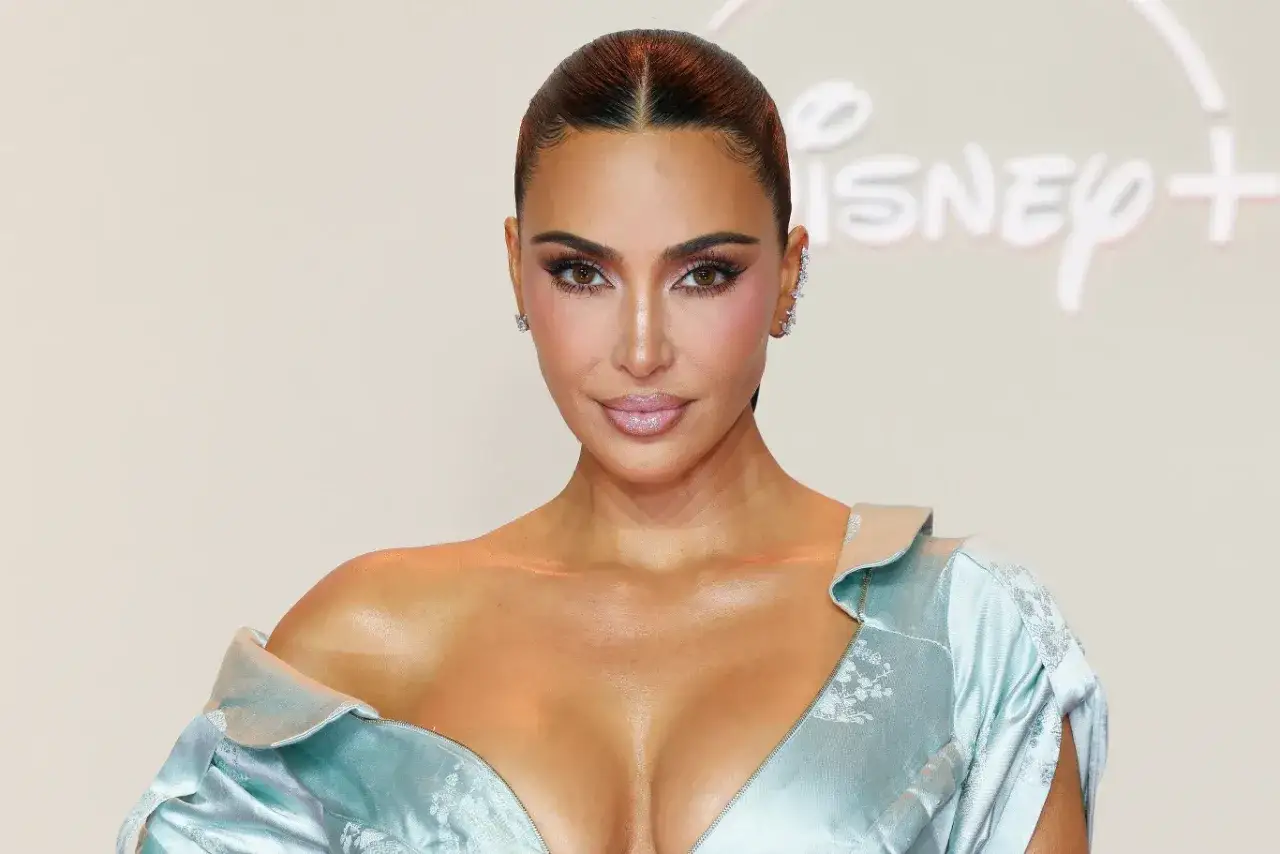 Kim Kardashian w błękitnej sukni, z błyszczącymi dodatkami. W tle logo Disney+. Ciekawe, ile lat ma Kim Kardashian, gdy nosi taką kreację?