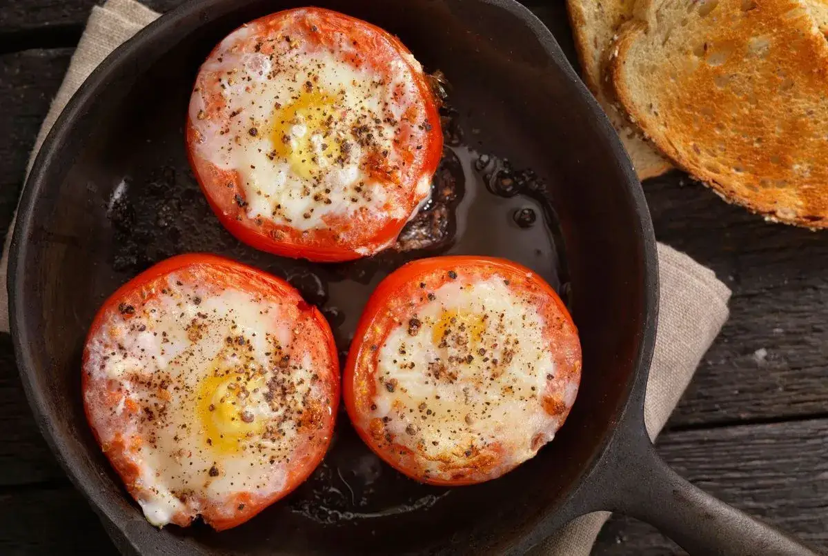 Trois œufs cuits dans des tomates, assaisonnés de poivre noir, dans une poêle en fonte. Un petit-déjeuner simple et savoureux : œuf tomate.