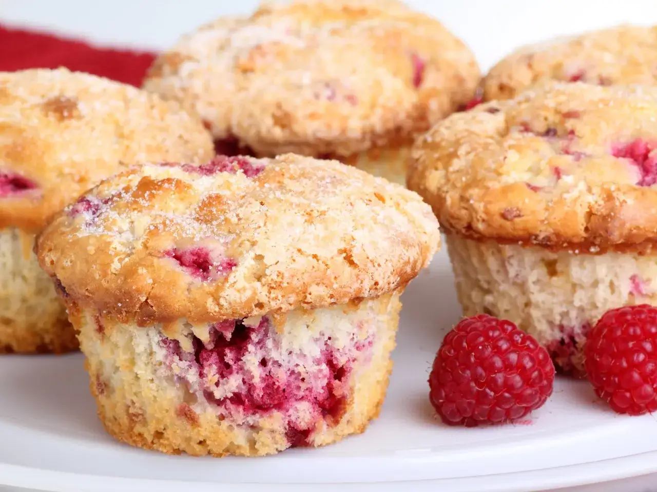 Saftige Himbeer Muffins, bestreut mit Zucker, auf einem Teller mit frischen Himbeeren.