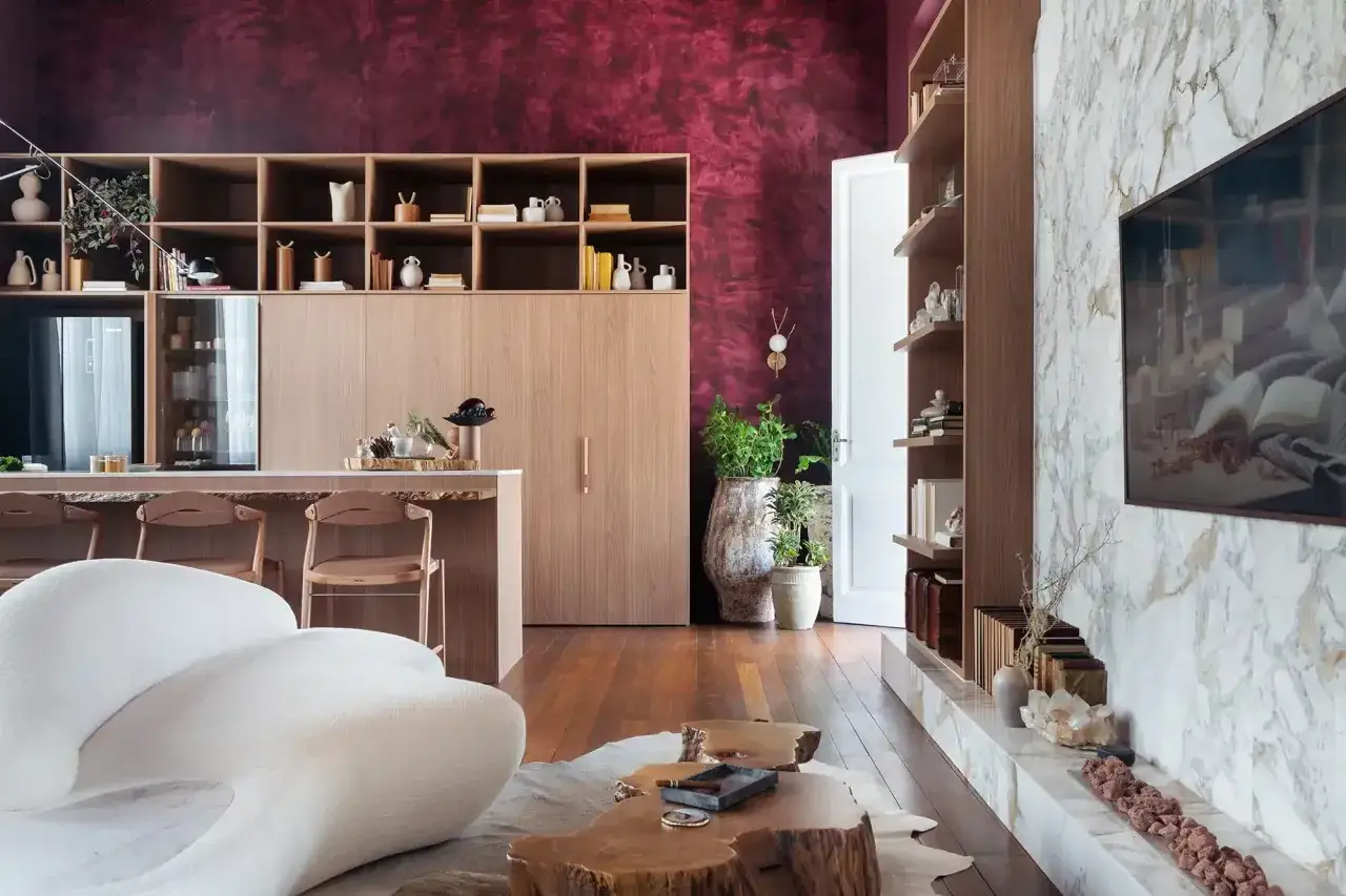 Eleganckie wnętrze z dominującym kolorem marsala na ścianie. Drewniane meble, biała sofa i marmurowy kominek tworzą przytulną atmosferę.