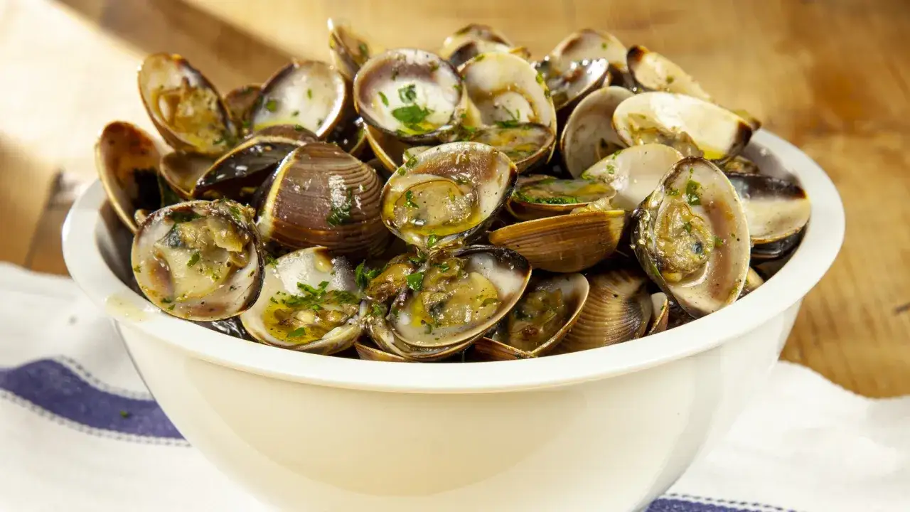 Un invitante saut&egrave; di vongole, profumato e succulento, servito in una ciotola bianca su un tavolo di legno.