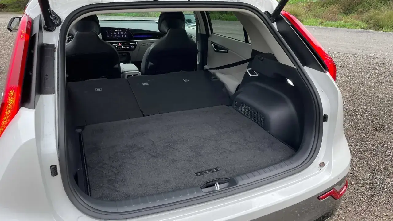 Pusta przestrzeń bagażowa Kia Niro EV, gotowa na podróż. Widok z tyłu na rozłożone siedzenia i dywanik z logo marki.