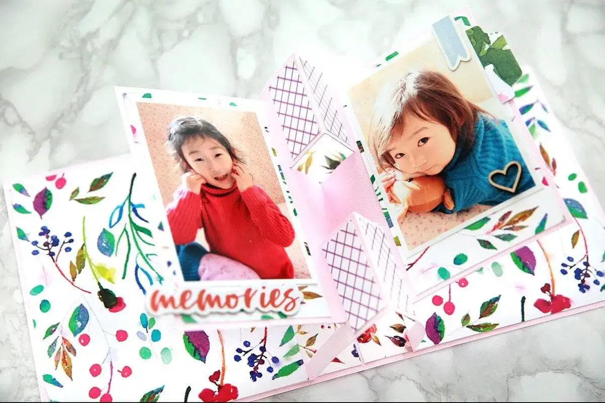 Oto przykład, co to jest scrapbooking: otwierana kartka z dwoma zdjęciami uroczych dziewczynek, ozdobiona akwarelowymi wzorami i napisem 