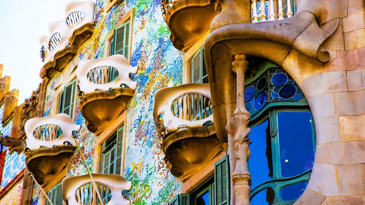 A vibrant facade showcasing Gaudi art, with colorful mosaic tiles, bone-shaped balconies, and a striking blue window.