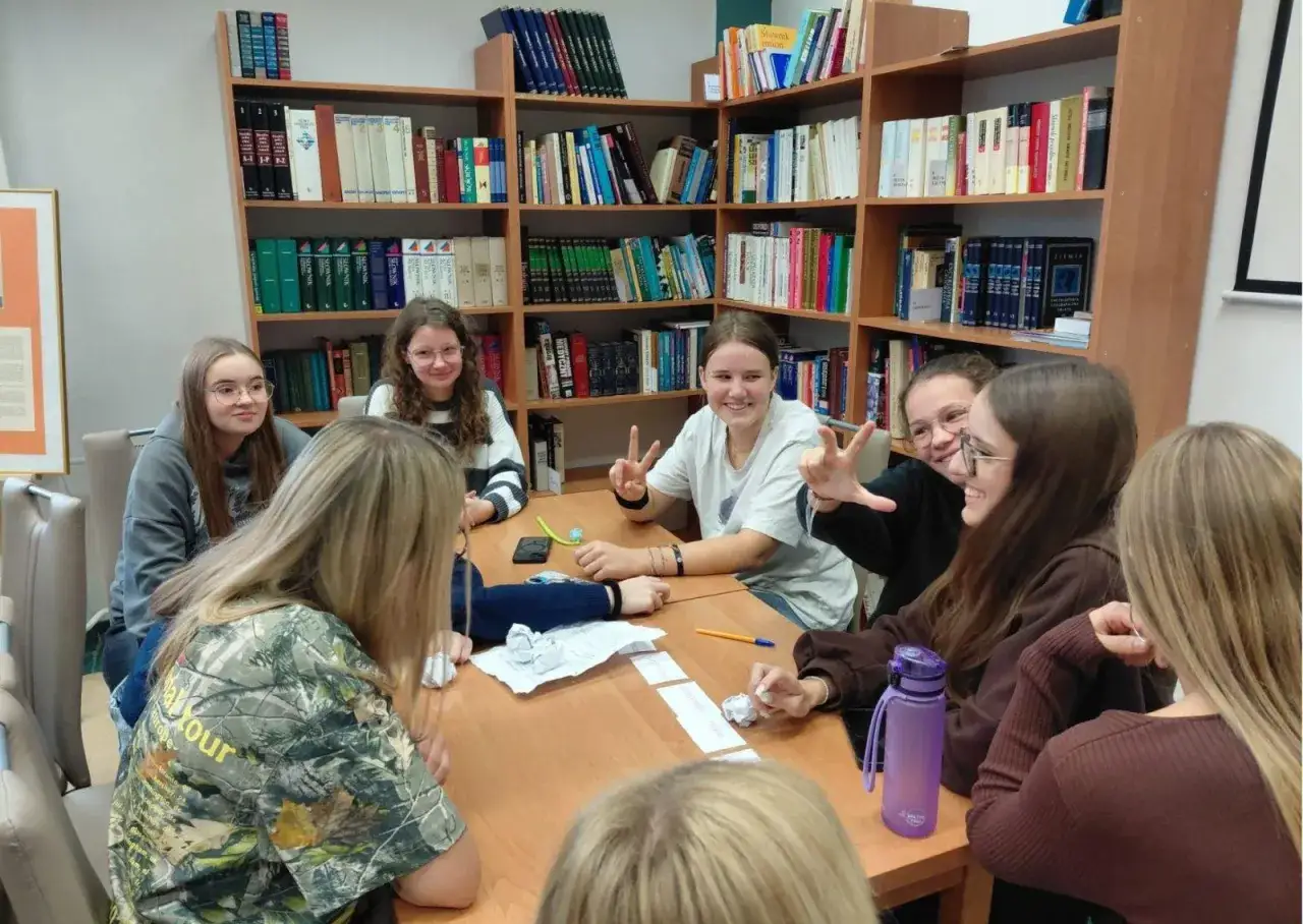 Uczennice dyskutują o tematach lekcji bibliotecznych w szkole średniej, siedząc przy stole w otoczeniu regałów z książkami.