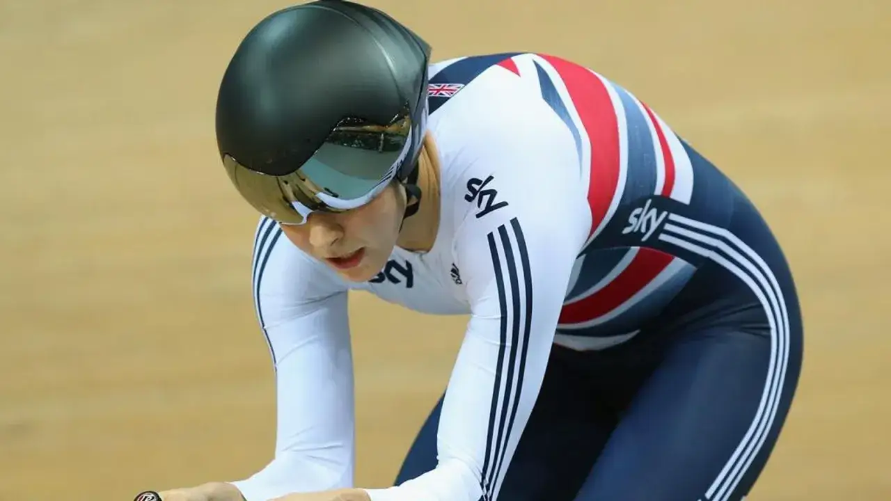 Joanna Rowsell, a British cyclist, in a white and Union Jack patterned skinsuit, wearing a black helmet and visor, focused on the track.