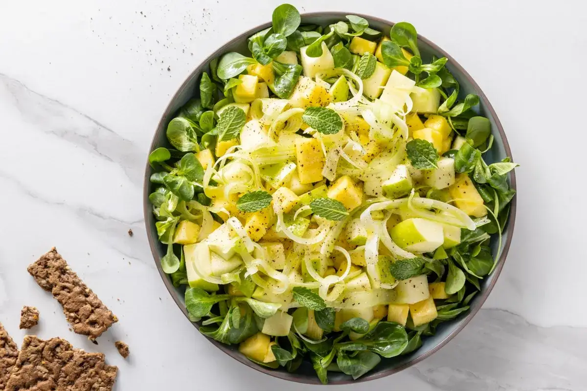 Insalata fresca e colorata con mela, ananas e finocchio, perfetta per piatti estivi veloci. Guarnita con menta e pepe.
