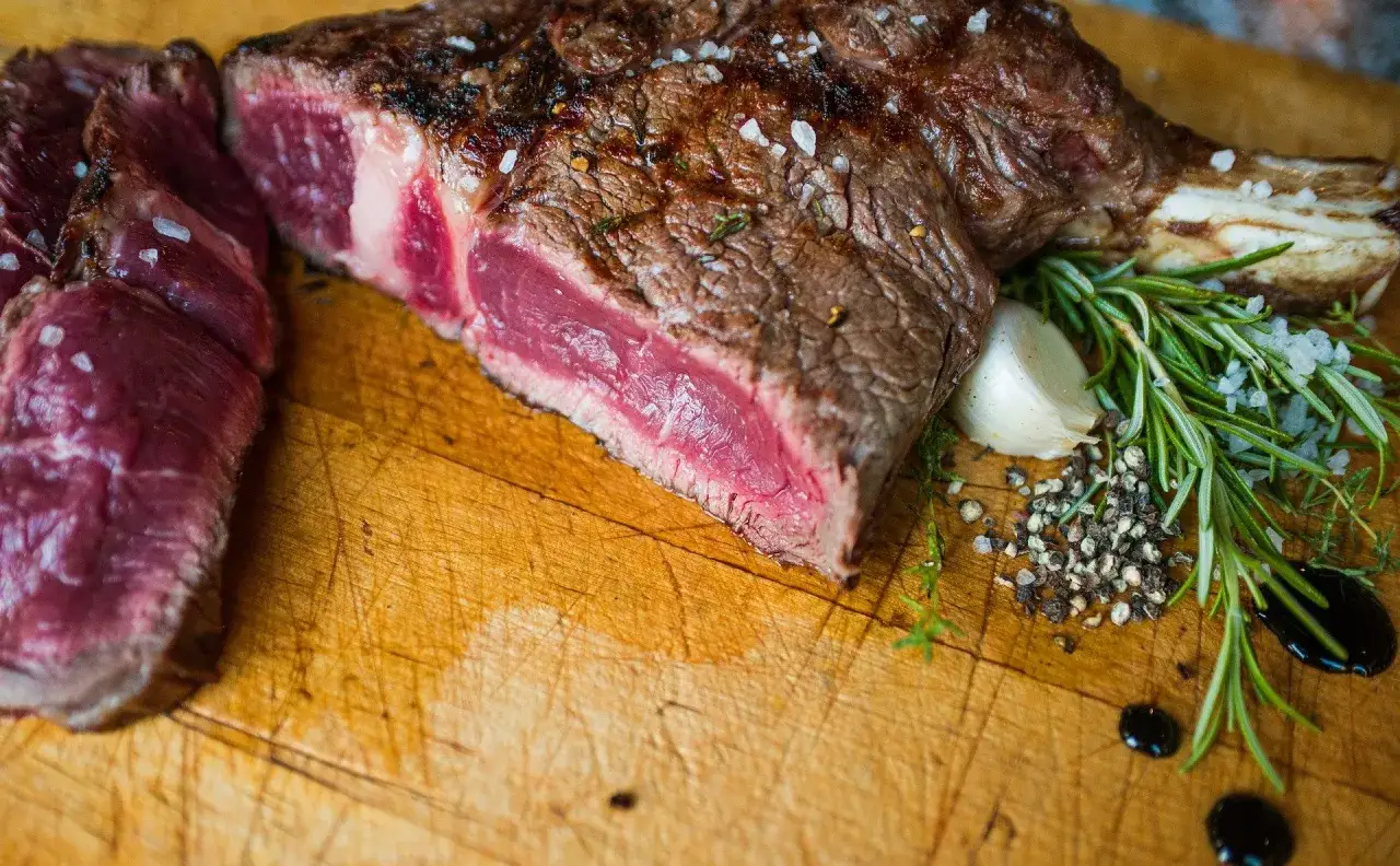 Une belle c&ocirc;te de b&oelig;uf saignante, assaisonn&eacute;e de gros sel et de poivre, avec une gousse d'ail et du romarin sur une planche en bois.