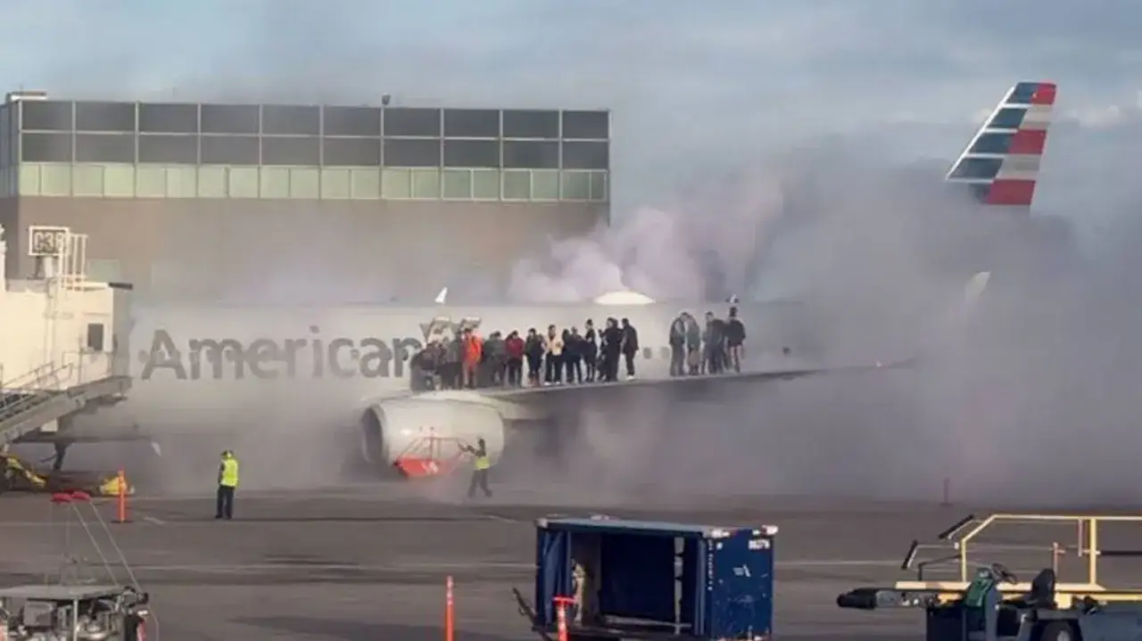 Pasażerowie stoją na skrzydle samolotu American Airlines, z którego wydobywa się dym. Wygląda to jak scena z ostatniej katastrofy samolotu pasażerskiego.