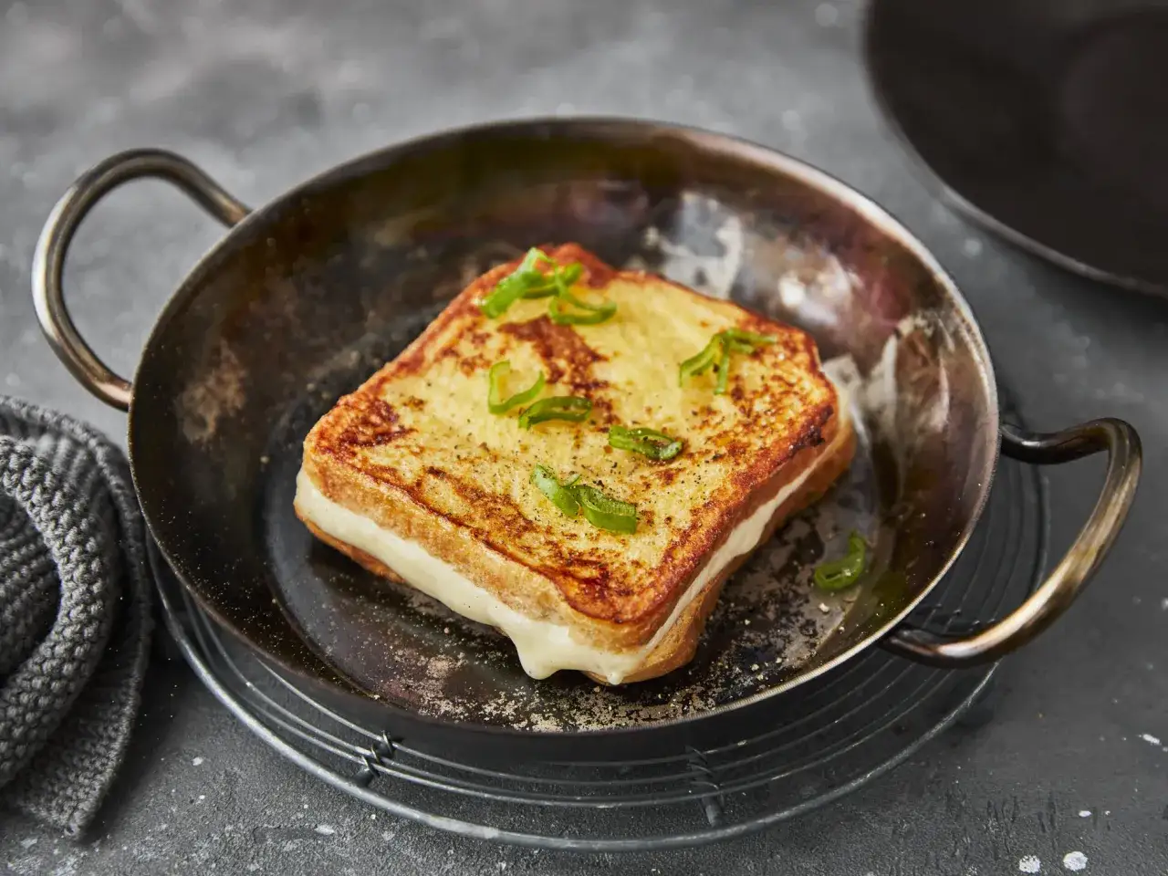 Herzhaftes French Toast mit geschmolzenem Käse und Frühlingszwiebeln in einer Pfanne.