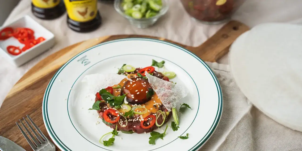 En läcker asiatisk råbiff med chili, salladslök och sesamfrön på en vit tallrik.