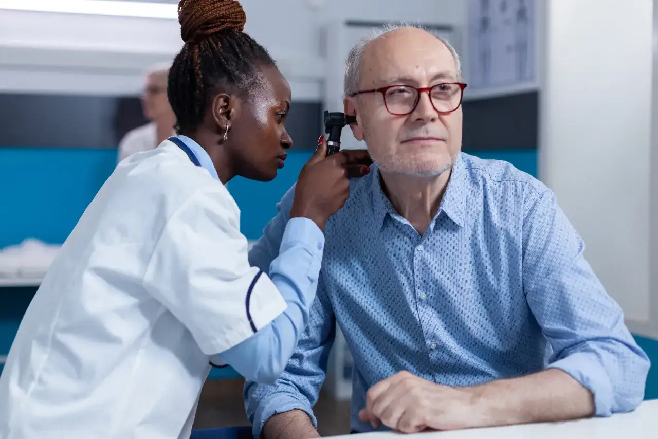 Une femme examine l'oreille d'un homme âgé avec un otoscope. Elle suit une formation audioprothésiste reconversion.