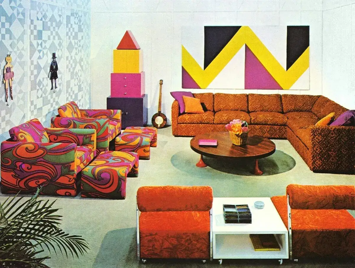 Ein Wohnzimmer im Retro-Stil mit bunten, psychedelischen Möbeln, einem großen Ecksofa und einem ovalen Couchtisch.