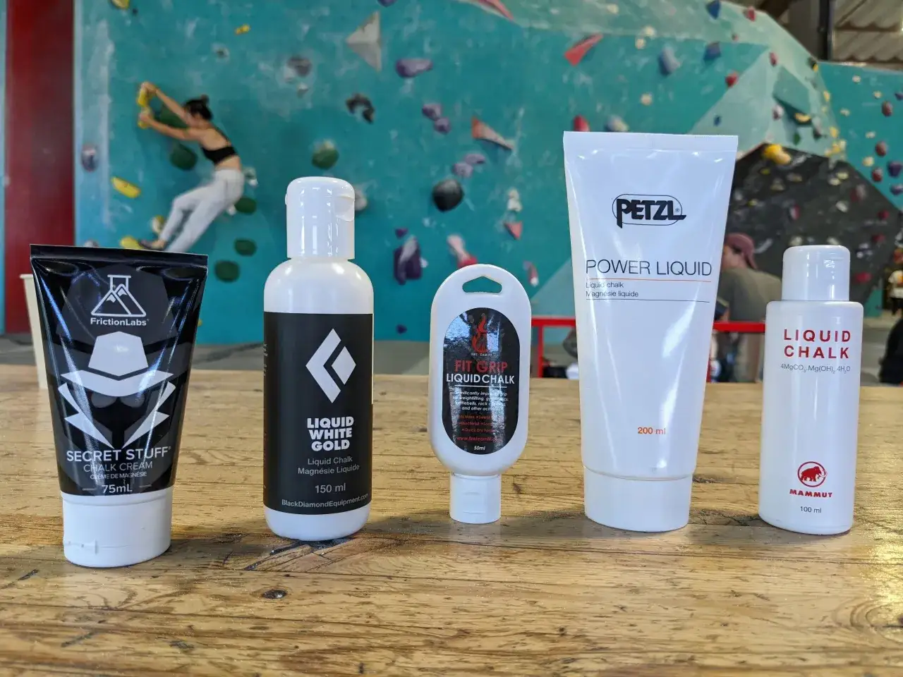 Cinco botellas de magnesio l&iacute;quido para escalada, con una escaladora en el fondo.