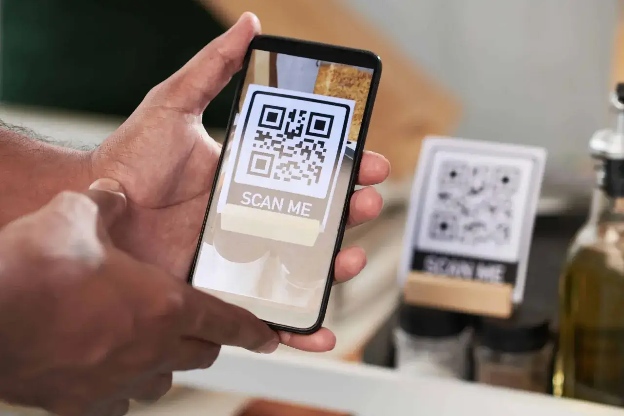 Ręka trzyma telefon, na ekranie którego widnieje kod QR z napisem 