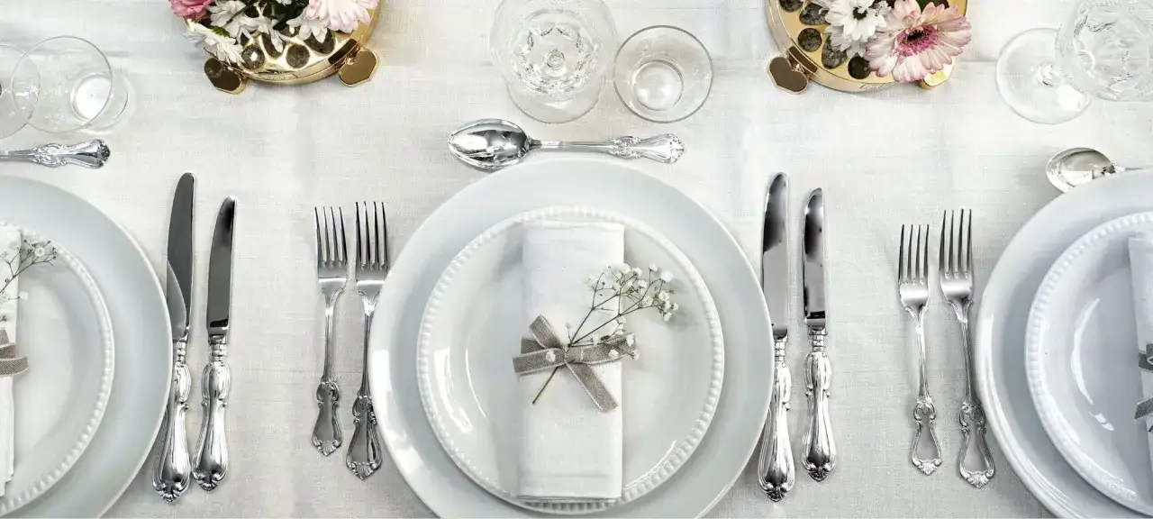 Vacker dukning med vita tallrikar, servetter dekorerade med blommor och elegant engångsbestick i silver.