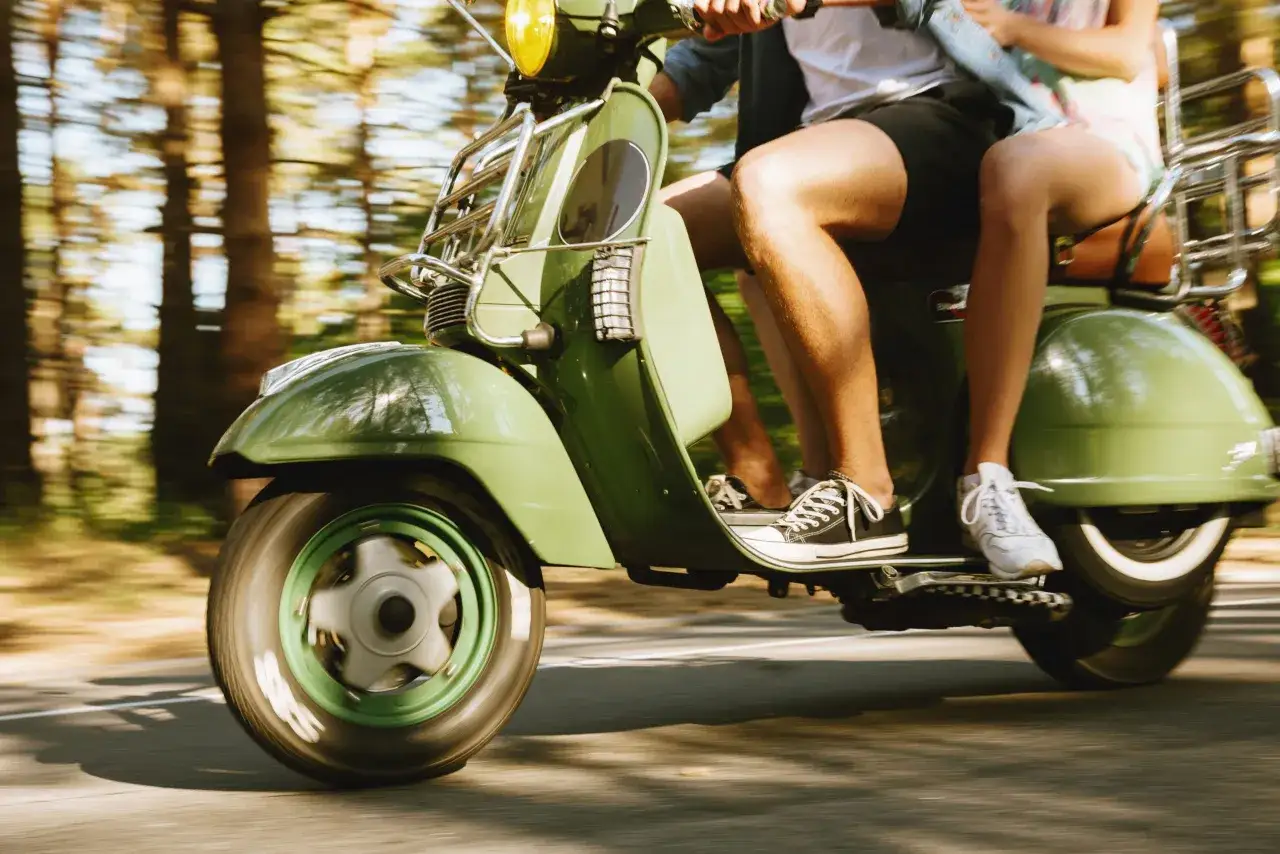 Zielony motorower pędzi przez las. Dwie osoby na nim, co to za wolność!
