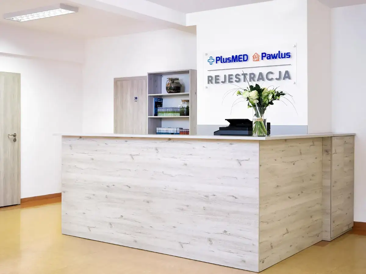 Recepcja w prywatnym centrum medycznym z logo PlusMED Pawlus i bukietem kwiatów.