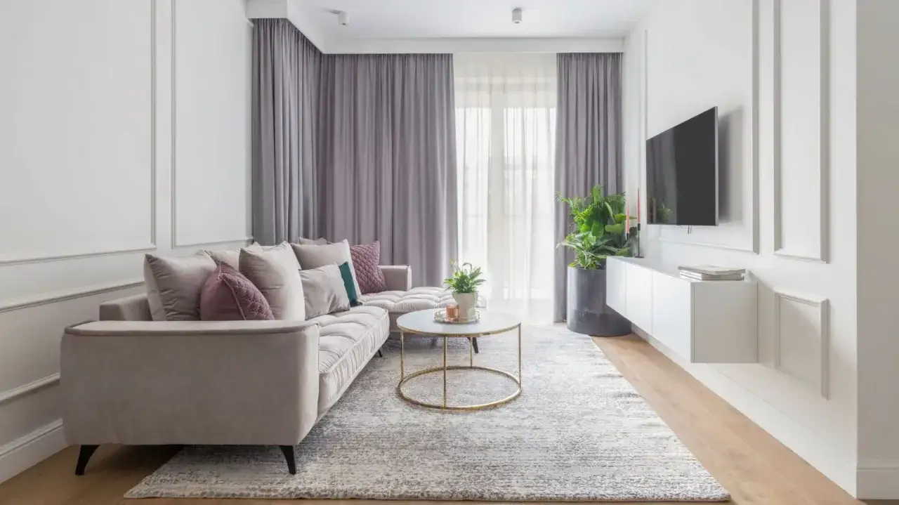 Elegancki salon w stylu modern classic z wygodną, beżową kanapą, okrągłym stolikiem kawowym i telewizorem na ścianie.