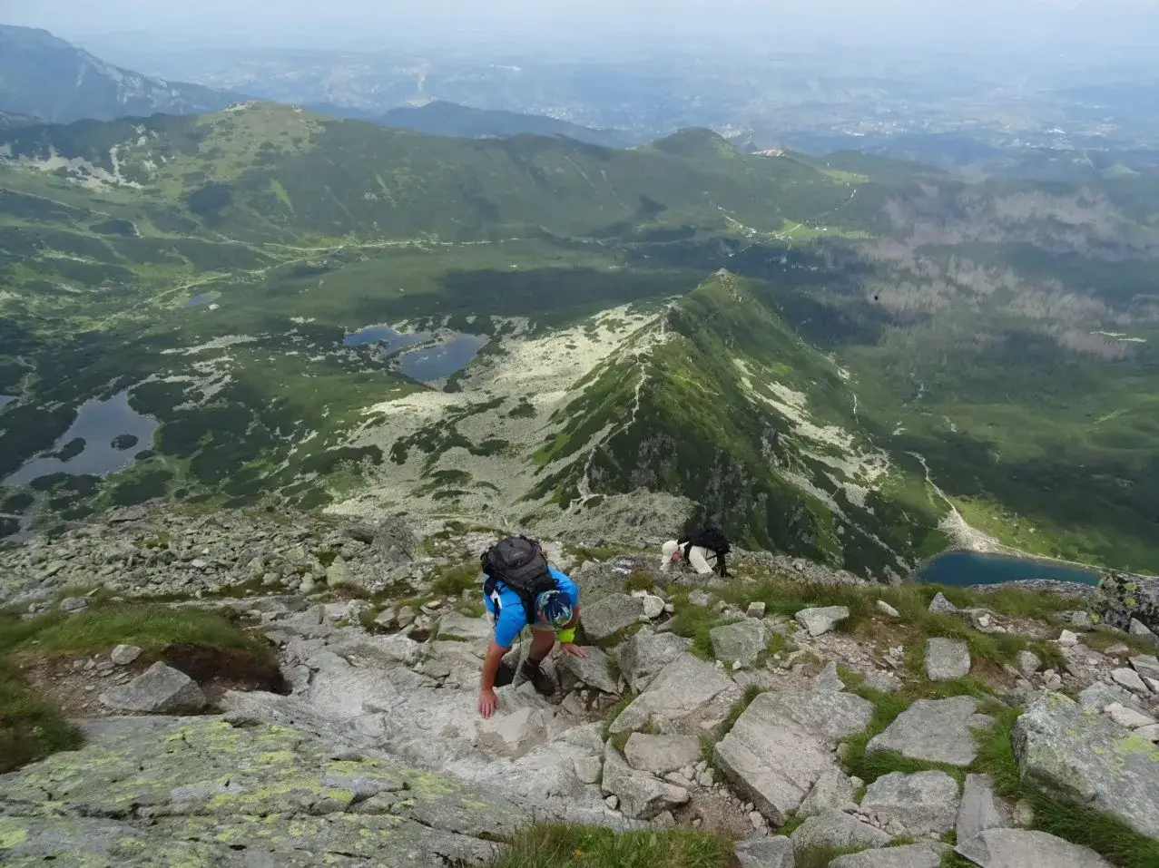 Turyści pokonują kamienisty szlak na Kościelec, podziwiając widok na Tatry i jeziora.