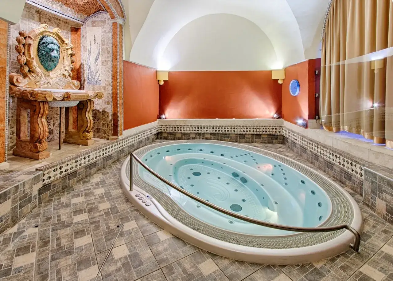 Luxuri&ouml;se Whirlpool-Anlage in einer Prager Therme, mit L&ouml;wenkopf-Dekor und warmen Wandfarben.