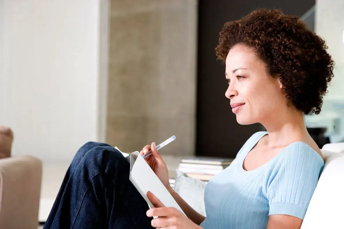 Mujer reflexiona escribiendo en su diario, un paso clave para saber como ser mejor persona.