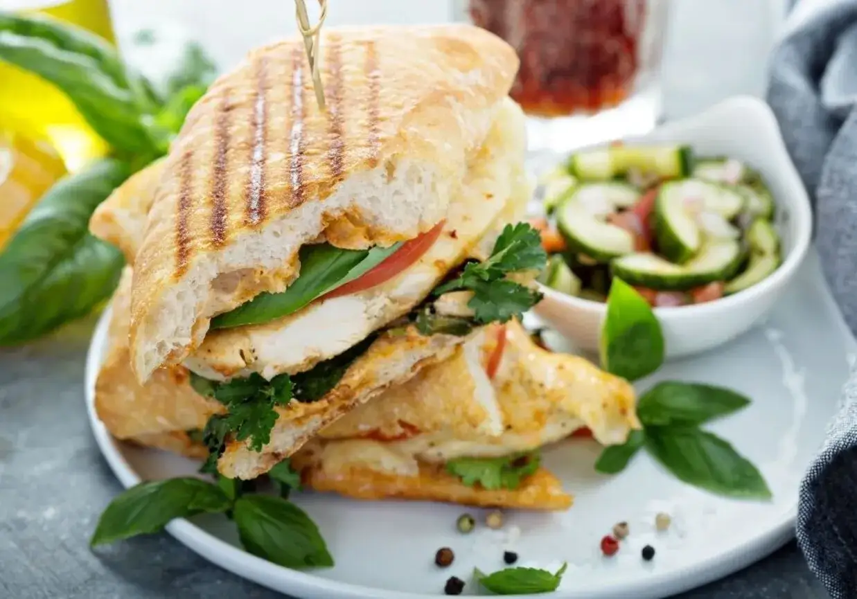 Pyszne panini z kurczakiem, pomidorem i bazylią, podane z sałatką z ogórka. Idealne na lekki posiłek.