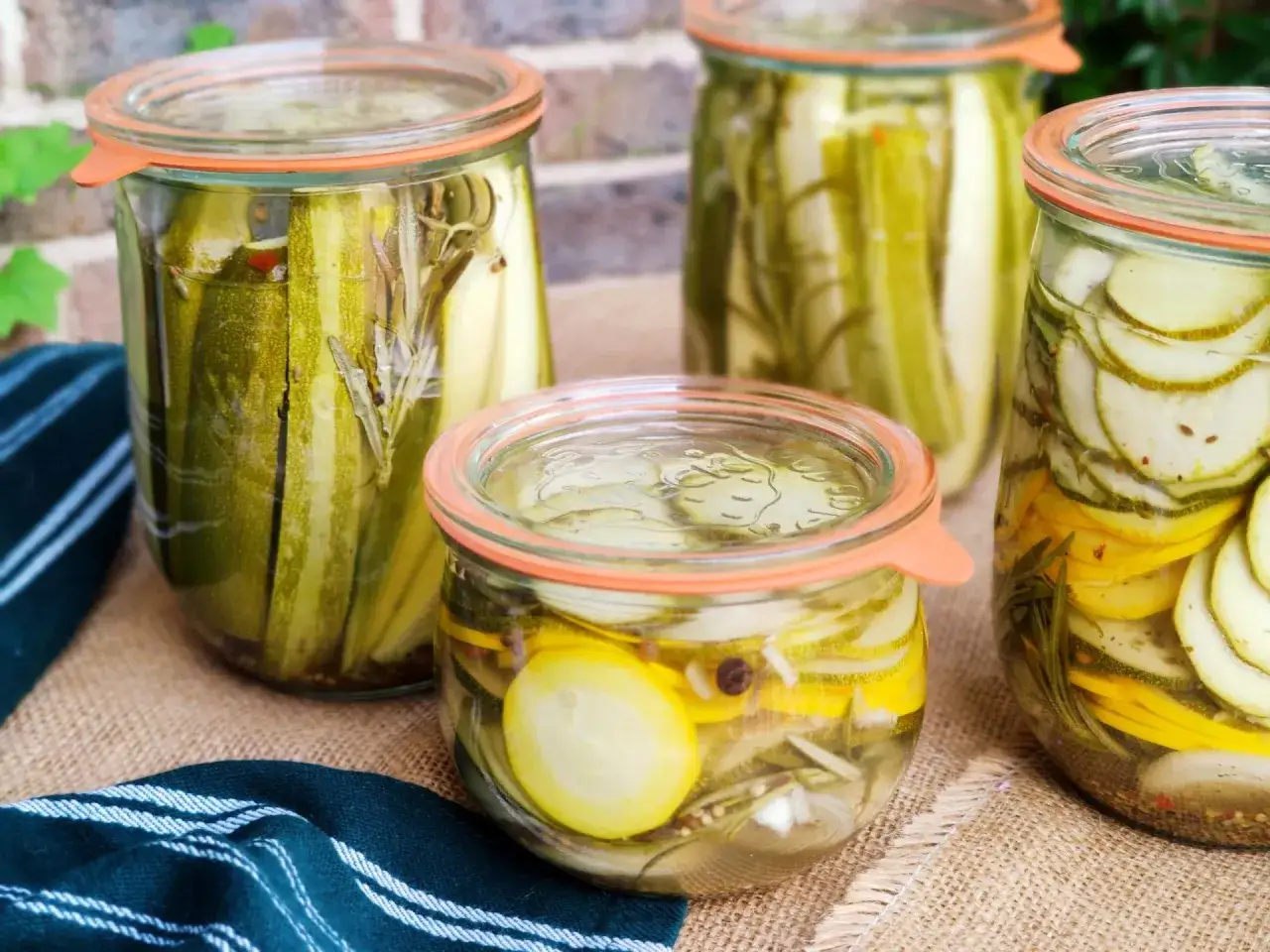 Zucchini einkochen: Gläser mit eingelegtem Gemüse, darunter Zucchini-Scheiben und ganze Zucchini, gefüllt mit Kräutern und Gewürzen.