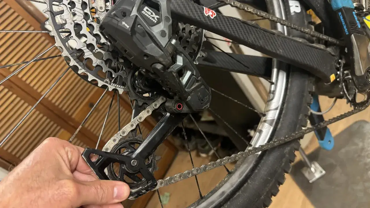 Close-up of a SRAM AXS setup on a mountain bike's rear derailleur and cassette. A hand is adjusting the derailleur.