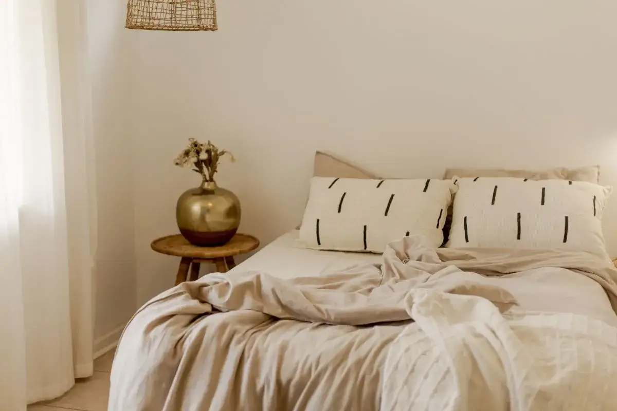 Cama con dos cojines de rayas negras, ropa de cama beige y un jarr&oacute;n dorado. La diferencia entre canap&eacute; y somier es que el canap&eacute; tiene cajones debajo.