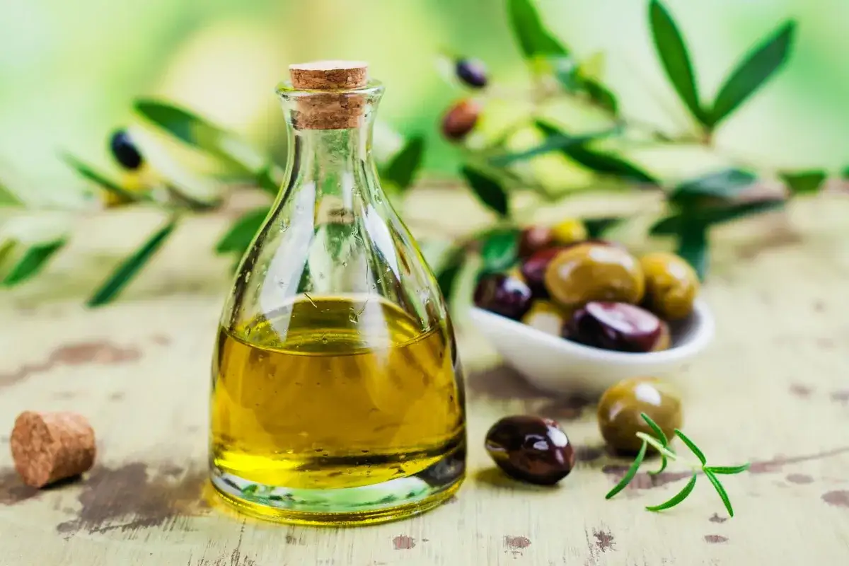 Olio di sansa in bottiglia di vetro, con olive miste e rametto di rosmarino. L'olio di sansa &egrave; commestibile e versatile in cucina.
