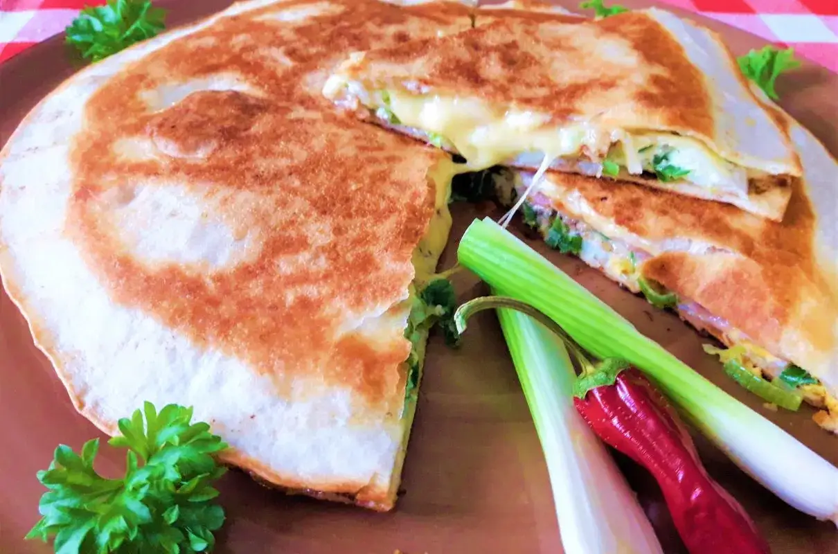 Gorąca tortilla z szynką i serem, roztopiony ser ciągnie się apetycznie. Podana z zieloną cebulką i papryczką.