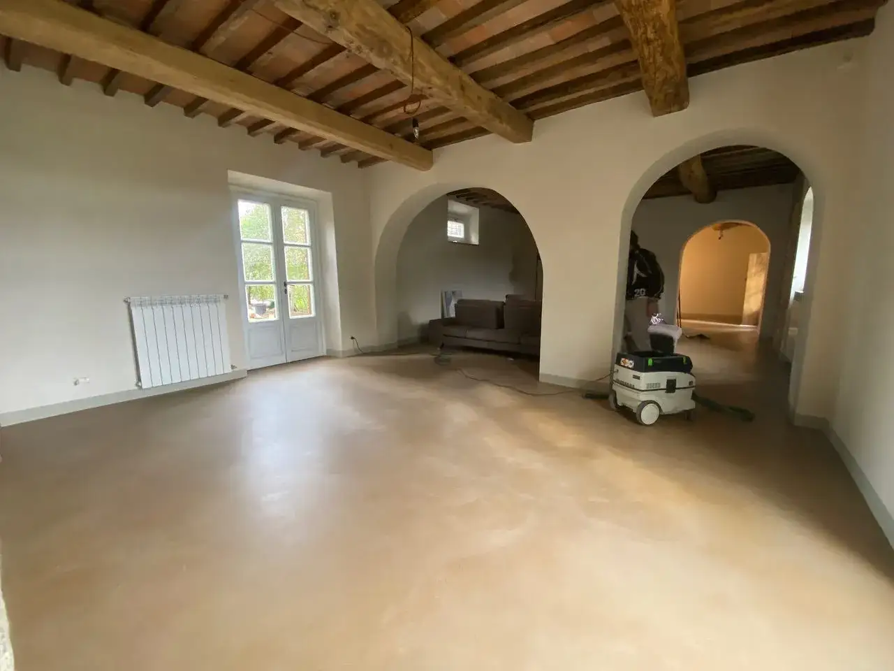Interno con travi a vista, porte finestre e un aspiratore pronto per la preparazione calce per imbiancare.
