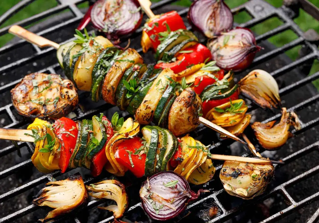 Szaszłyki warzywne z cukinii, papryki i ziemniaków pieczone na grillu, otoczone grillowaną cebulą.