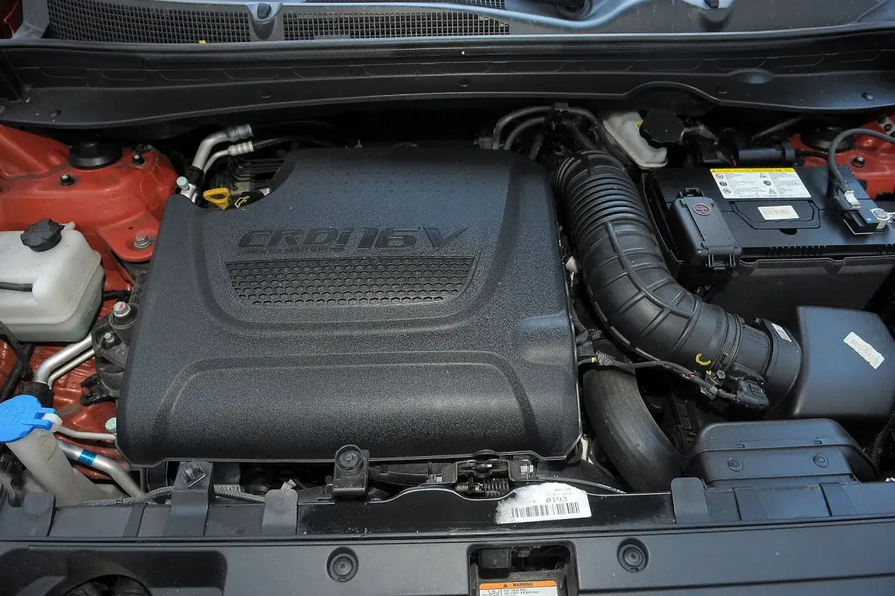 Silnik CRDi 16V w Kia Sportage 2015. Widoczny akumulator, wąż dolotowy i płyn do spryskiwaczy.
