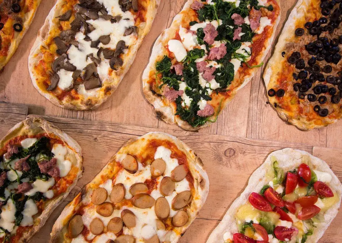 Plusieurs pizzas italiennes aux garnitures variées : champignons, épinards et saucisse, olives, saucisses, tomates cerises.