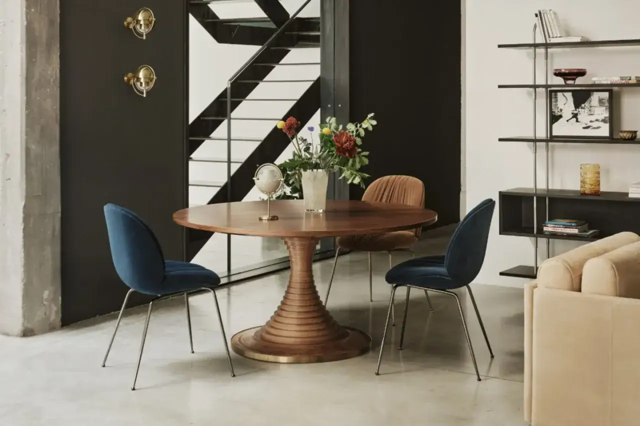 Stilvolle Wohnung inspo: Ein runder Holztisch mit vier Samtstühlen in Blau und Braun, daneben ein Bücherregal und ein Sofa.