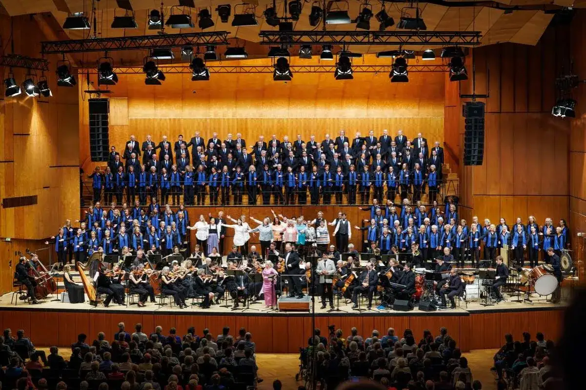 Großer Chor und Orchester auf einer Bühne. Ein Dirigent steht vor ihnen. Dies ist ein Beispiel dafür, was ist eine Operette: eine musikalische Darbietung mit Gesang und Schauspiel.