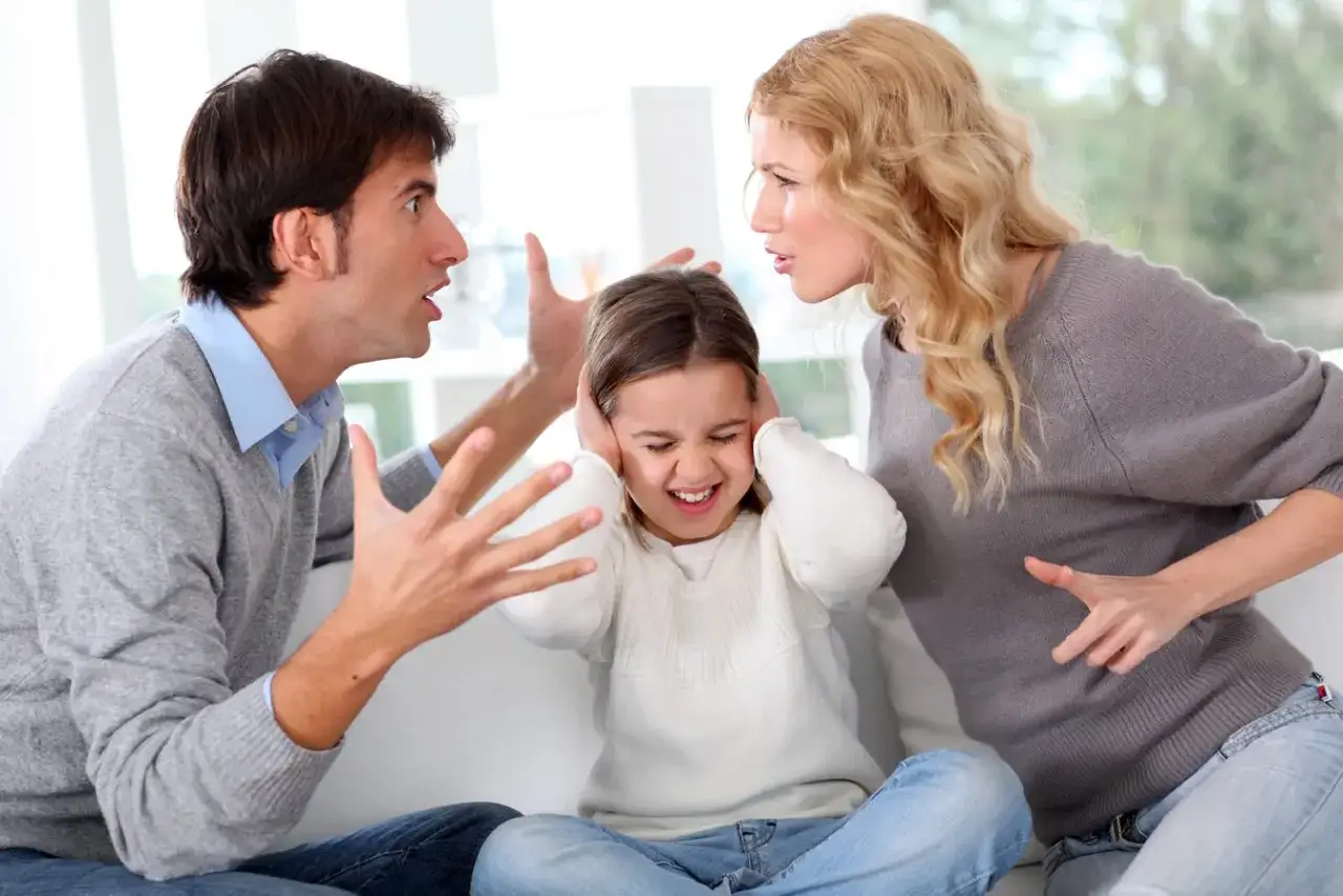 Una bambina si tappa le orecchie mentre i genitori separati litigano animatamente.