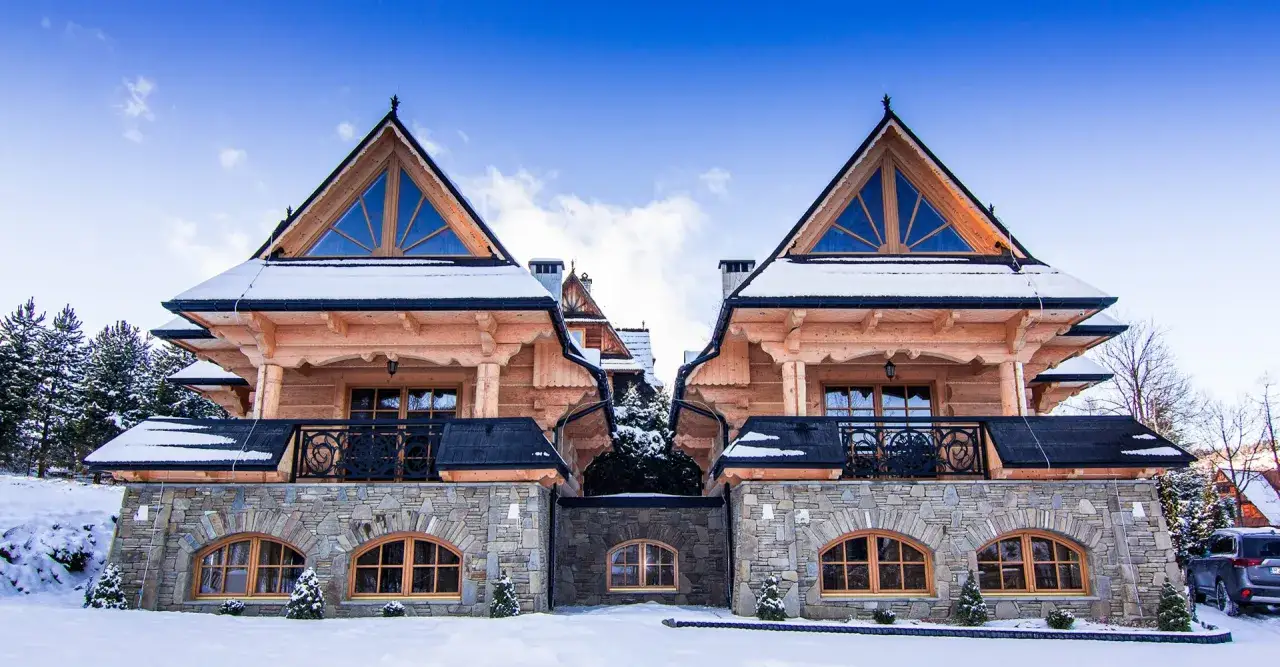 Zimowy widok na zakopane pensjonat pod Giewontem. Drewniane domy z kamienną podstawą, pokryte śniegiem, pod błękitnym niebem.