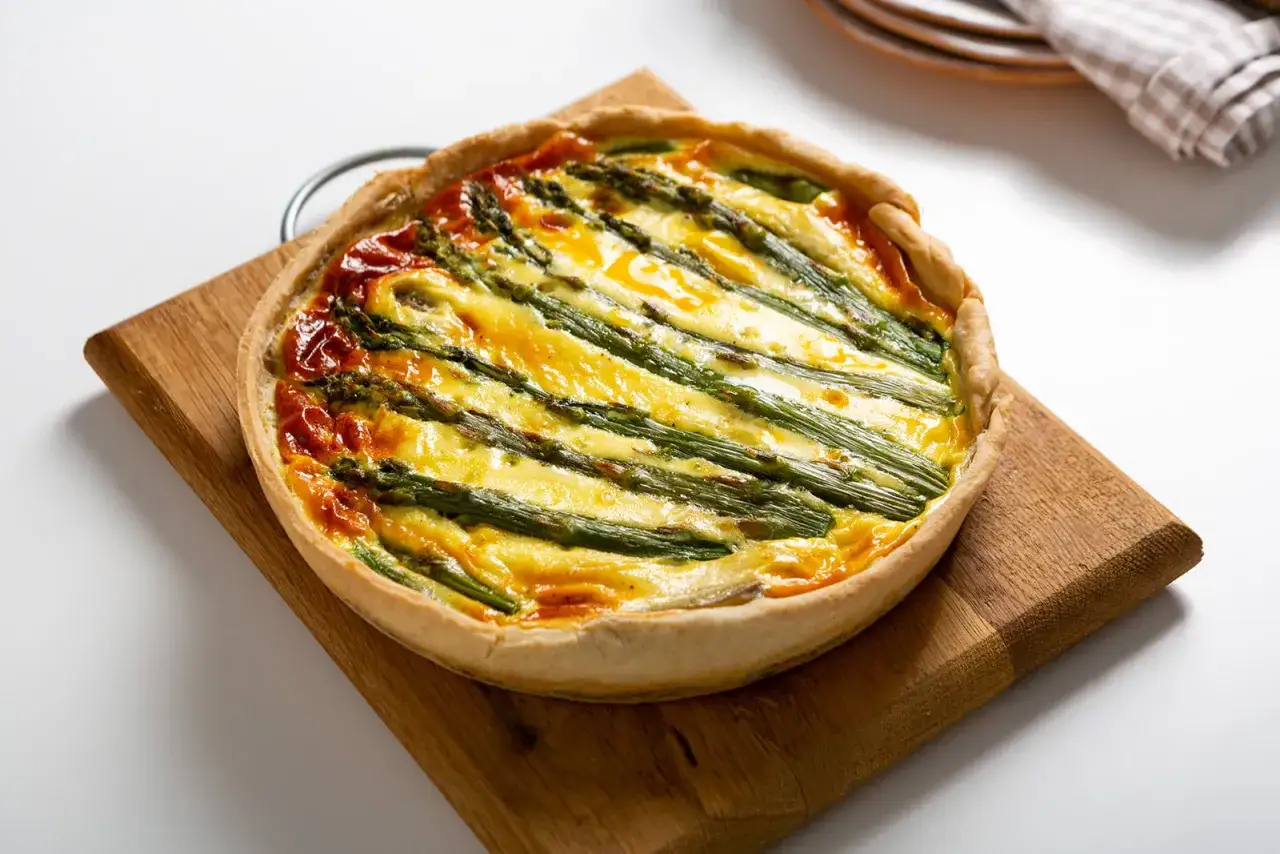 Eine köstliche Spargel Quiche mit goldgelbem Käse und knackigem Spargel auf einem Holzbrett.