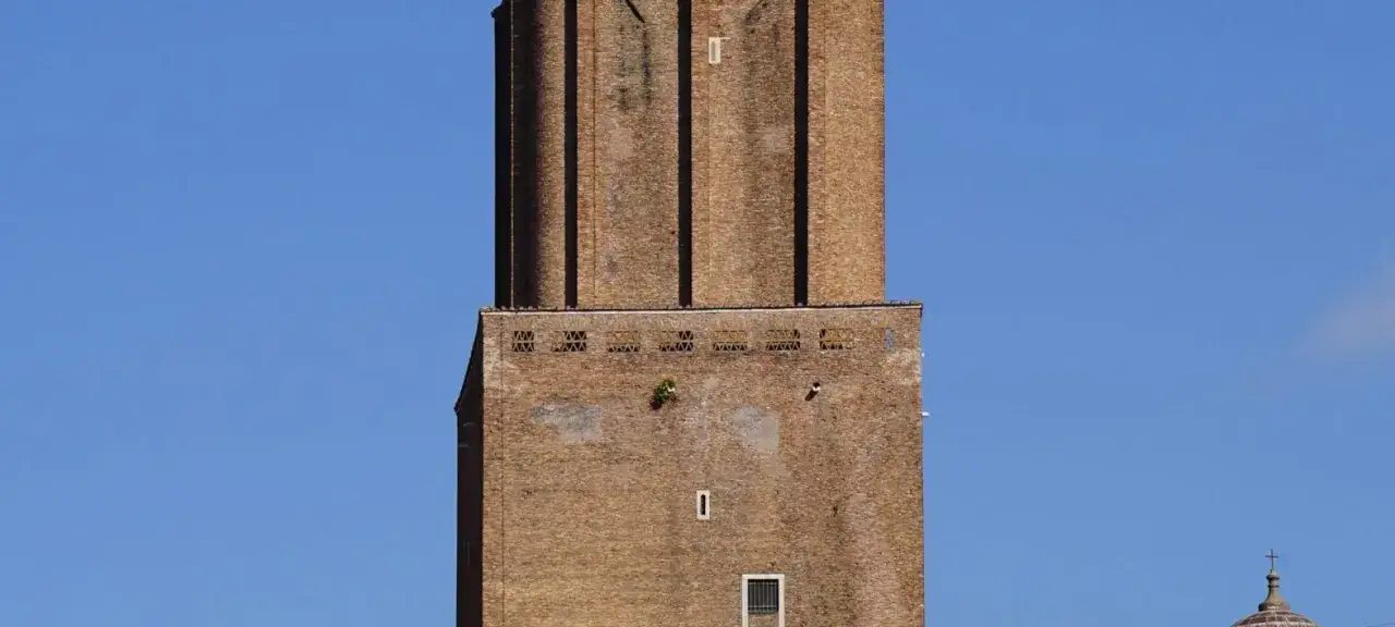 La torre delle Milizie si erge maestosa contro il cielo azzurro. La sua struttura in mattoni rossi presenta finestre e decorazioni che raccontano storie antiche.