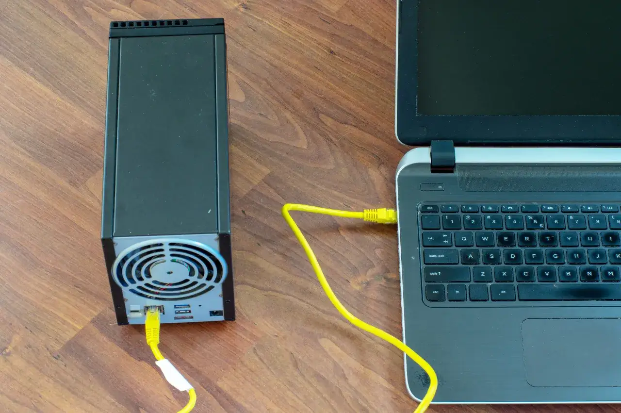 Ein gelbes Netzwerkkabel verbindet einen Synology NAS direkt mit einem Laptop.