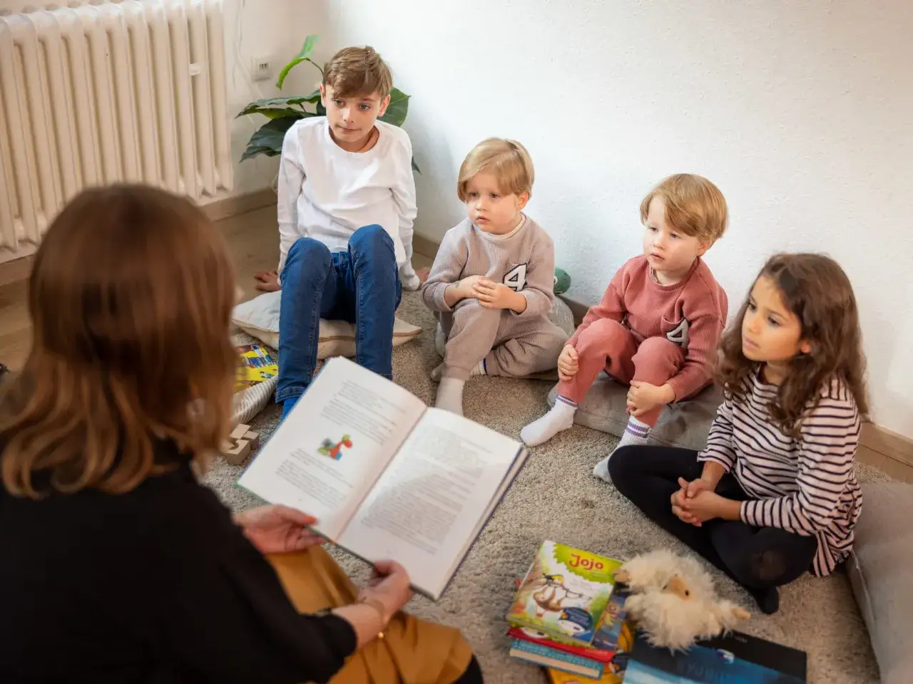 Alle Kinder lernen lesen: Eine Frau liest vier Kindern auf dem Teppich eine Geschichte vor.