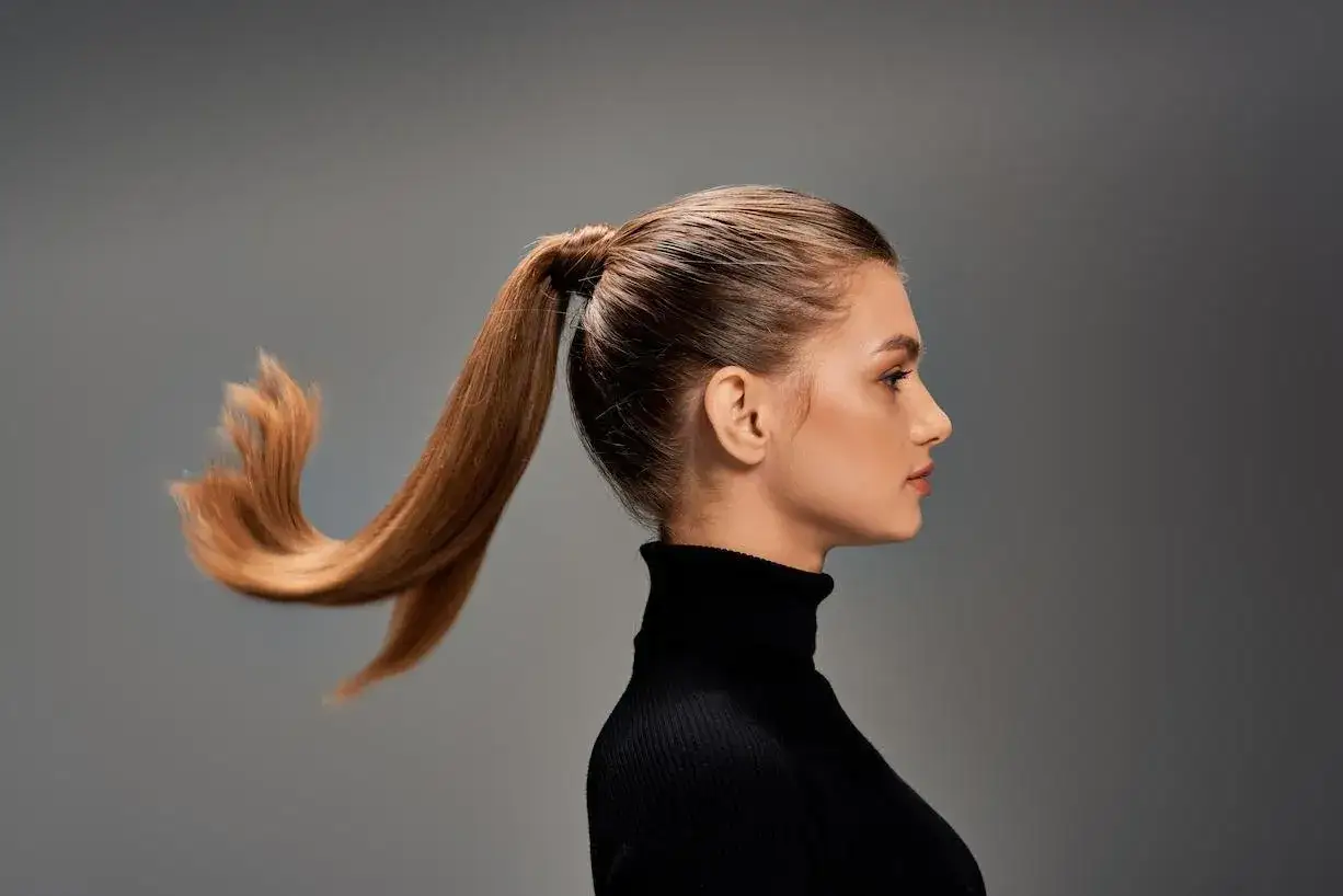 Mujer con coleta alta y cabello castaño moviéndose con el viento, luciendo un suéter negro de cuello alto.