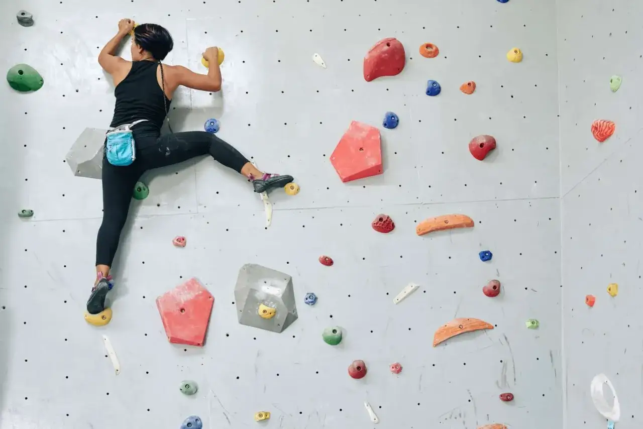 Une femme en pleine escalade sur un mur coloré, concentrée sur sa prochaine prise.