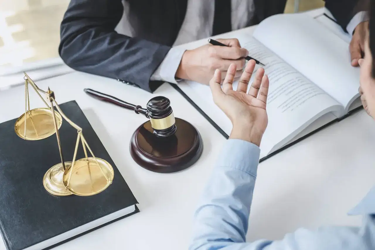 Prawnik i klient dyskutują, czy prace społeczne można zamienić na grzywnę. Na stole waga sprawiedliwości, księga i młotek sędziowski.
