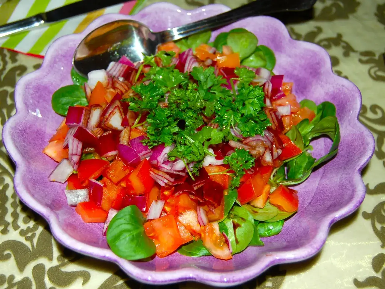 En f&auml;rgglad sallad shirazi med tomater, r&ouml;dl&ouml;k och persilja i en lila sk&aring;l.