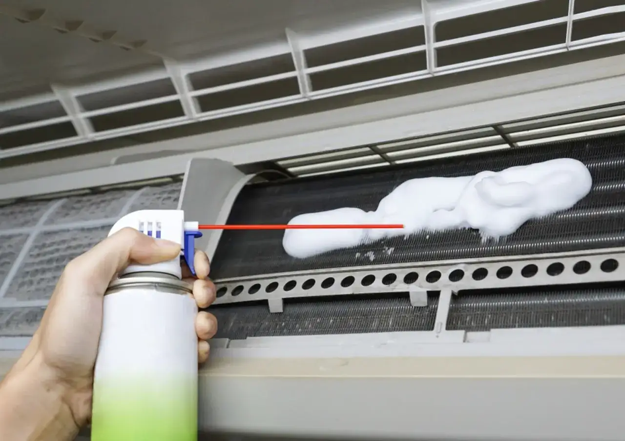 Limpieza del evaporador del aire acondicionado con espuma. Un spray limpia las aletas metálicas del aparato.
