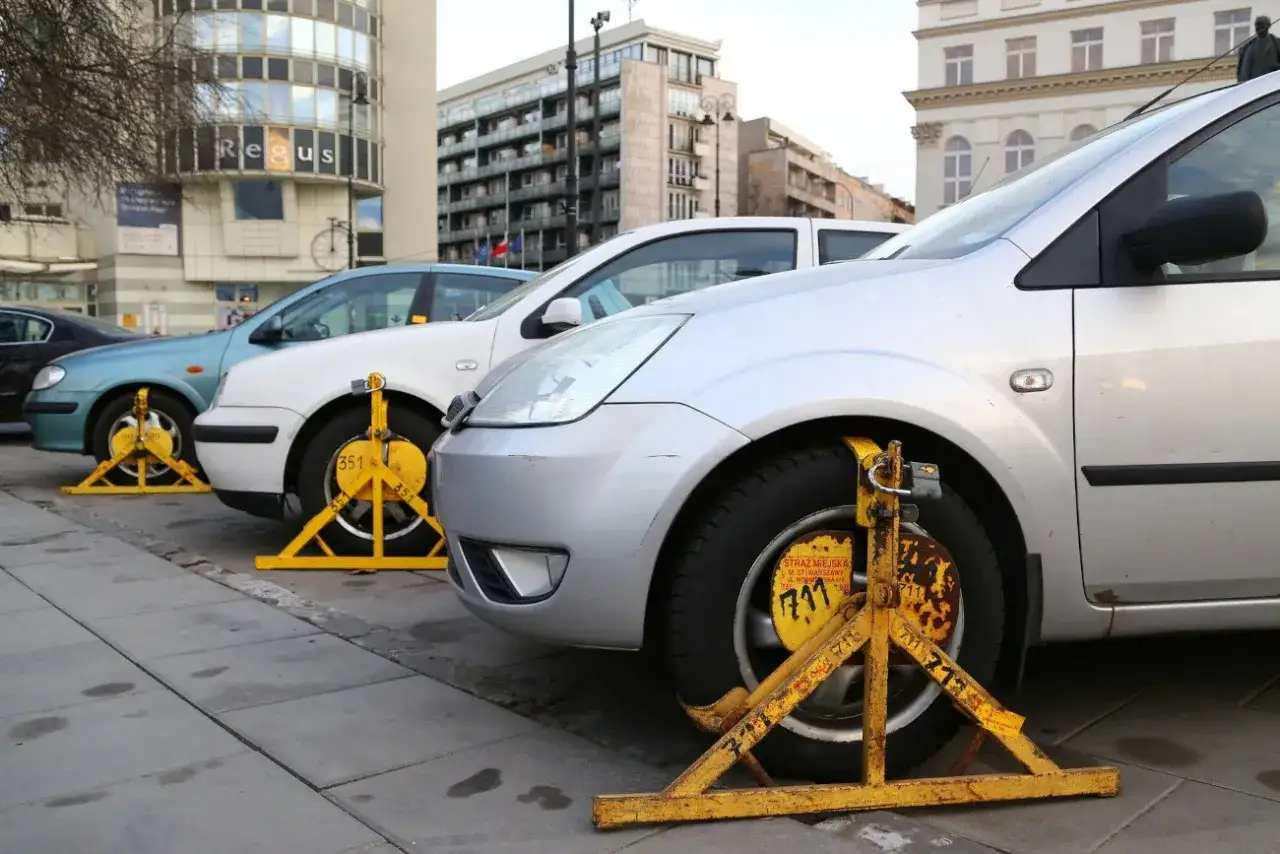 Samochody z założonymi blokadami na kołach, znak nielegalnego parkowania na chodniku.